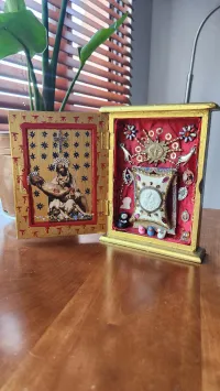 Mixed media work made from painted yellow box with charms pinned to red interior. 